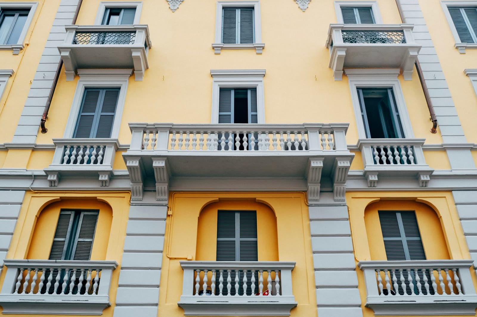 Facciata gialla di un palazzo residenziale italiano con balconi in pietra e persiane grigie