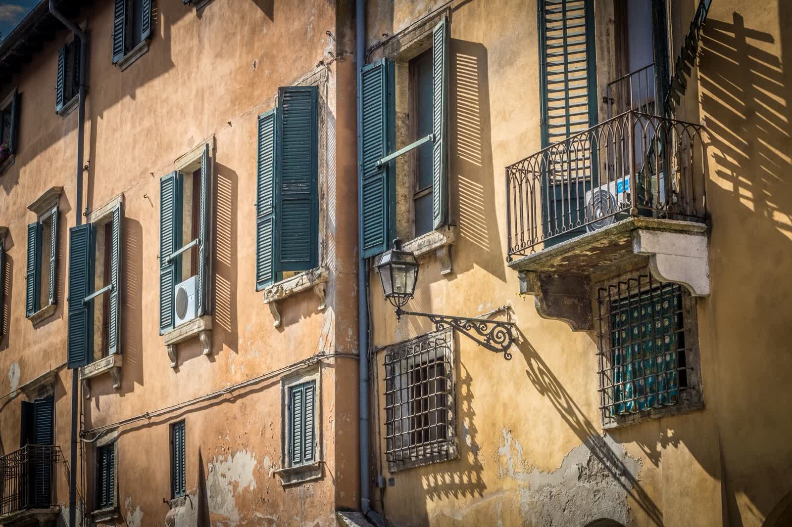 Facciata di un vecchio palazzo residenziale italiano a Verona, con intonaco scrostato, persiane verdi e un balcone in ferro battuto