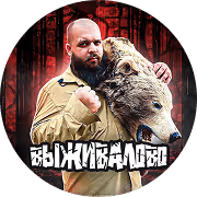 Мужчина с бородой и бритой головой в светло-коричневой рубашке держит кожаную маску с головой волка на фоне тёмного леса.