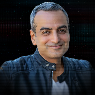 Smiling woman with short dark hair wearing small hoop earrings and a black beaded necklace against a dark background.