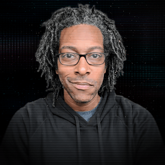 Smiling man with glasses and beard wearing a blue button-up shirt against a dark background.