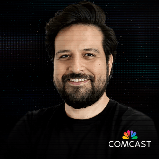 Smiling man with dark hair and beard wearing a black shirt with Comcast logo on the bottom right corner.
