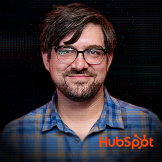 Smiling young woman with long light brown hair, wearing a gray shirt and gold necklace against a dark digital background.