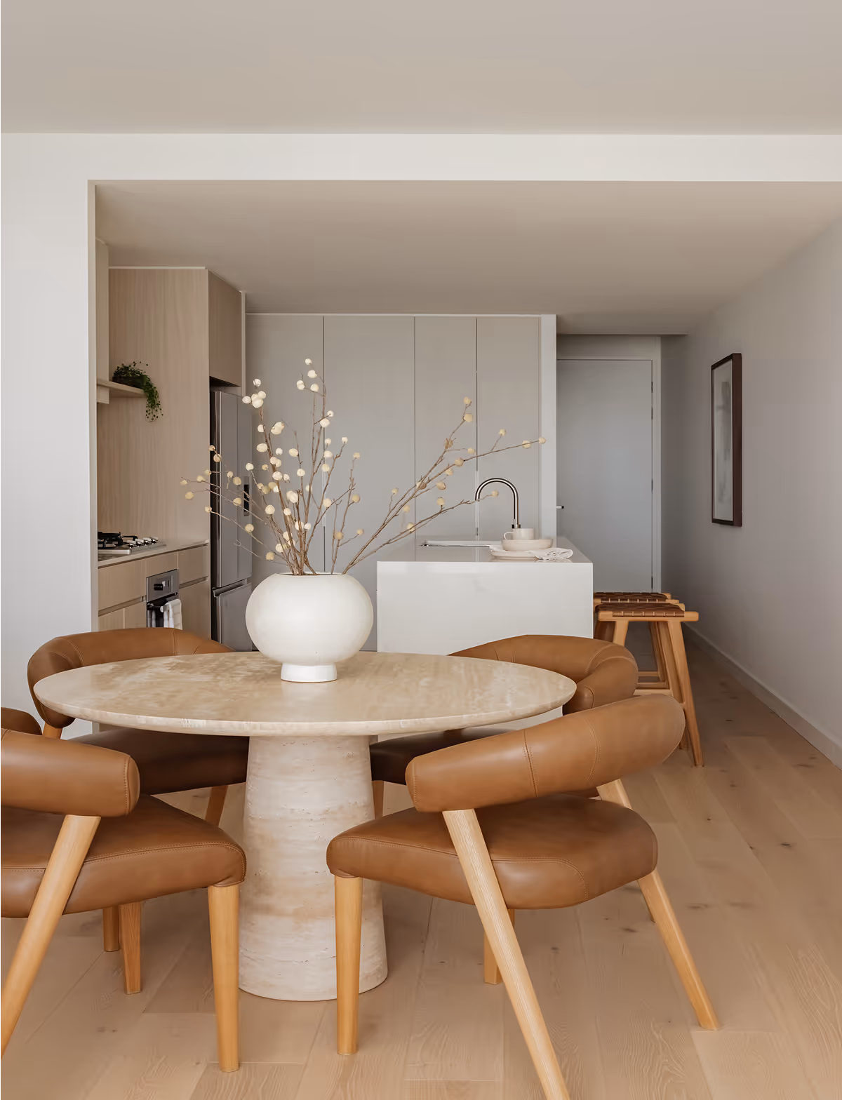 Modern kitchen with white cabinetry, marble backsplash, three beige bar stools, and a blurred figure walking behind the island.