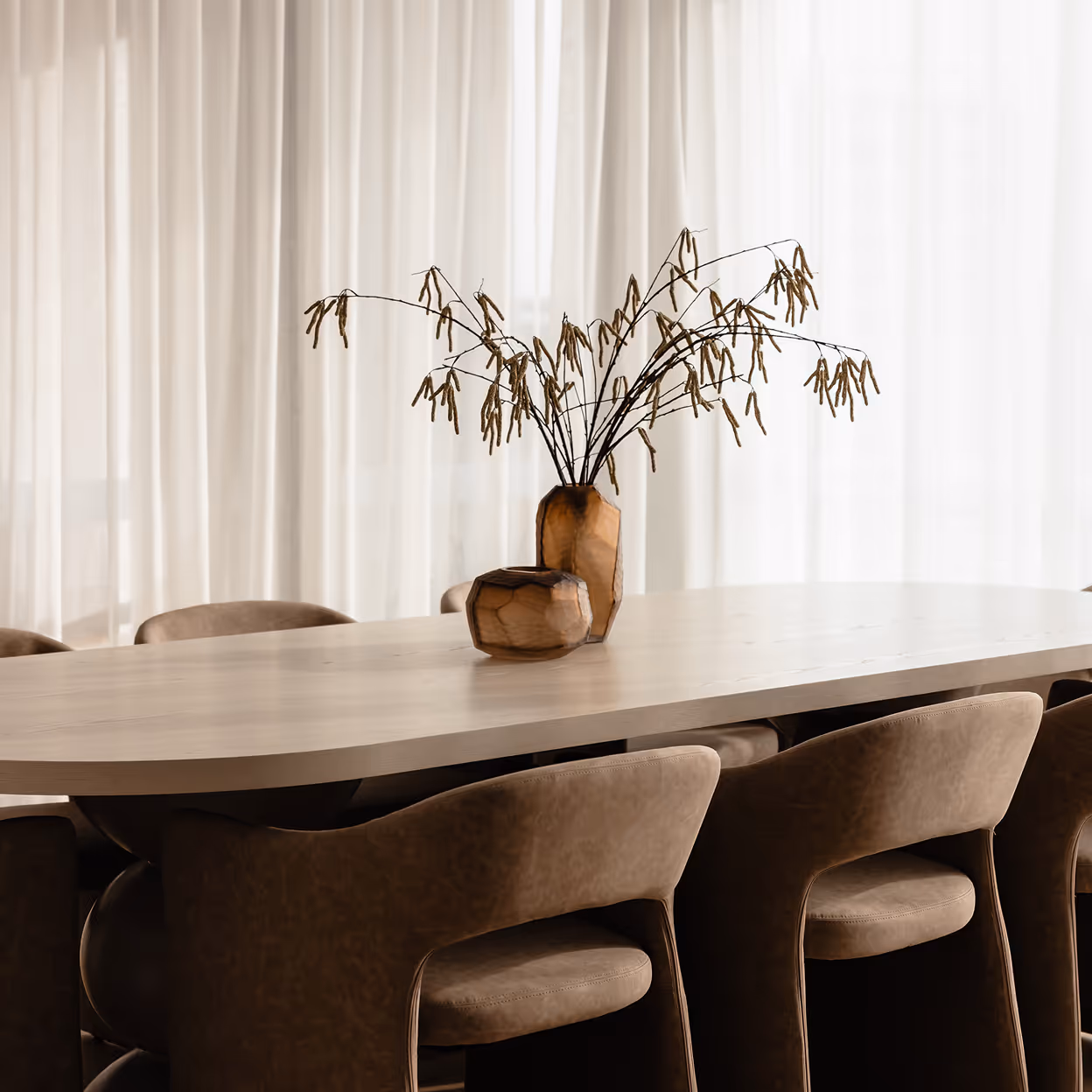 Modern living room corner with a beige armchair, white pillow, white side table, potted plant, and flat-screen TV on a white cabinet against a white paneled wall.