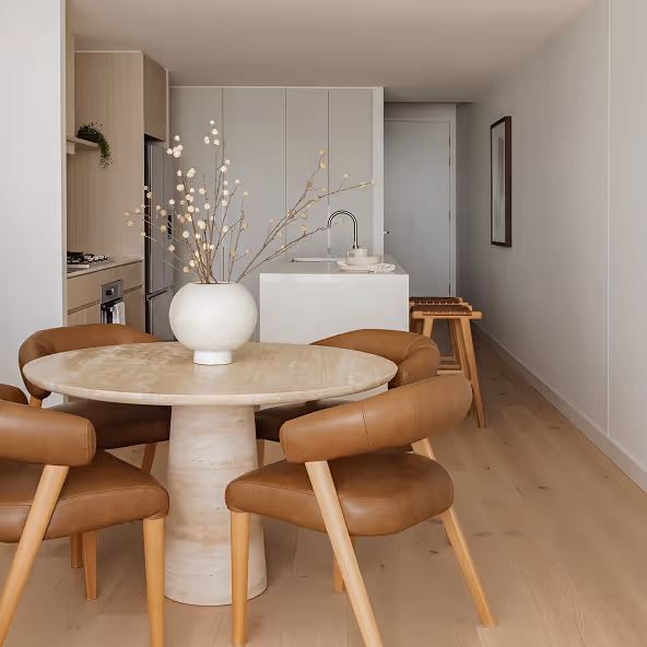 Corner section of a brown leather sofa with three decorative pillows and a beige throw blanket draped on the armrest.
