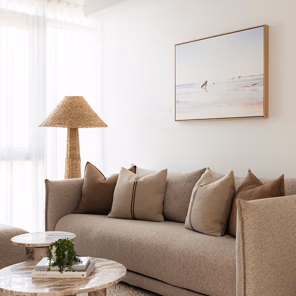 Two neatly made beds with gray and white pillows and blankets, separated by a nightstand with a white lamp.