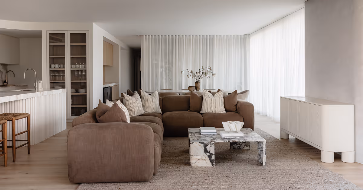 Modern living room with brown sectional sofa, marble coffee table, white cabinet, and sheer curtains.
