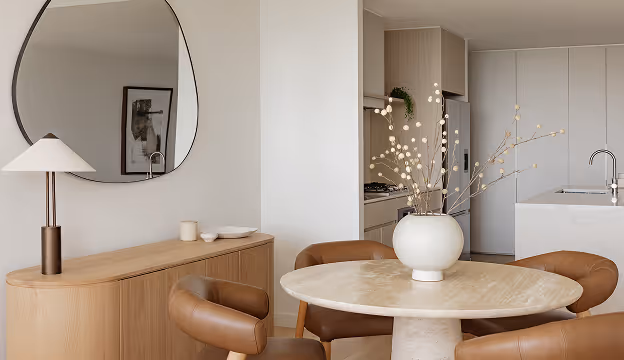 Minimalist dining room with round table, brown chairs, sideboard, lamp, and oval wall mirror.
