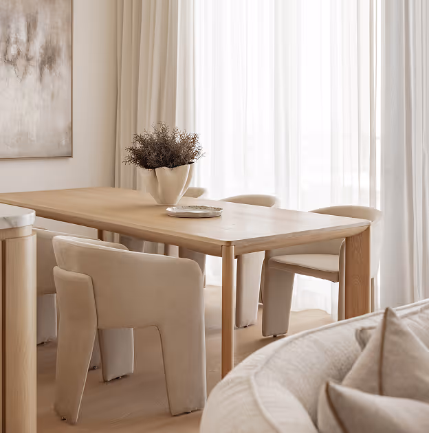 Minimalist dining area with wooden table, beige chairs, a decorative vase, and sheer white curtains.
