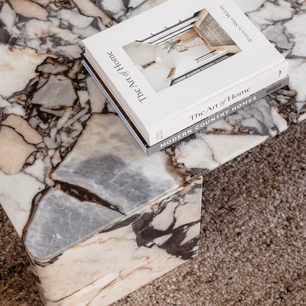Marble table with beige, gray, and black veining holding two stacked home decor books.