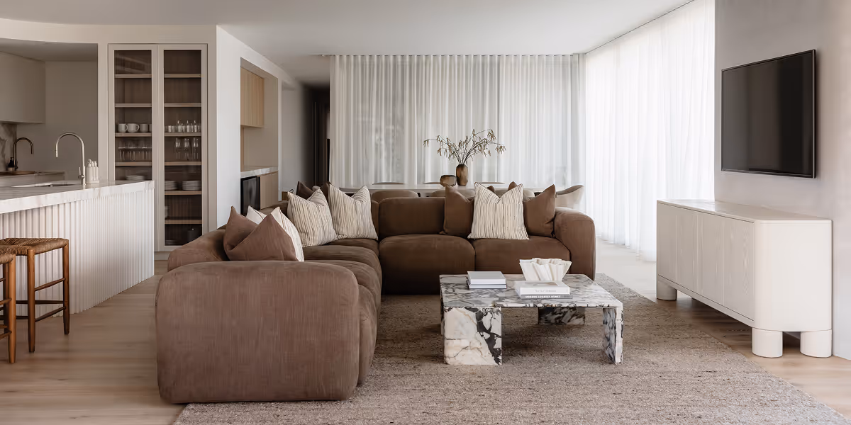 Modern living room with brown sectional sofa, marble coffee table, white media console, and open kitchen.