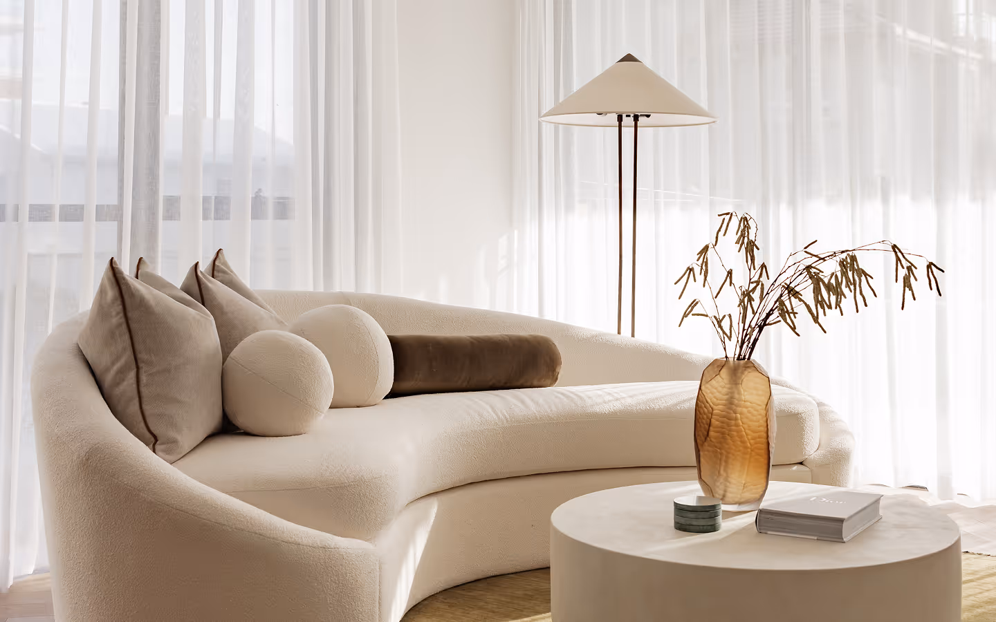 Minimalist dining table with beige chairs, ceramic vase with dried branches, and soft sheer curtains.