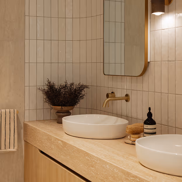 Modern bathroom counter with two round sinks, brass faucet, mirror, and decorative plant.