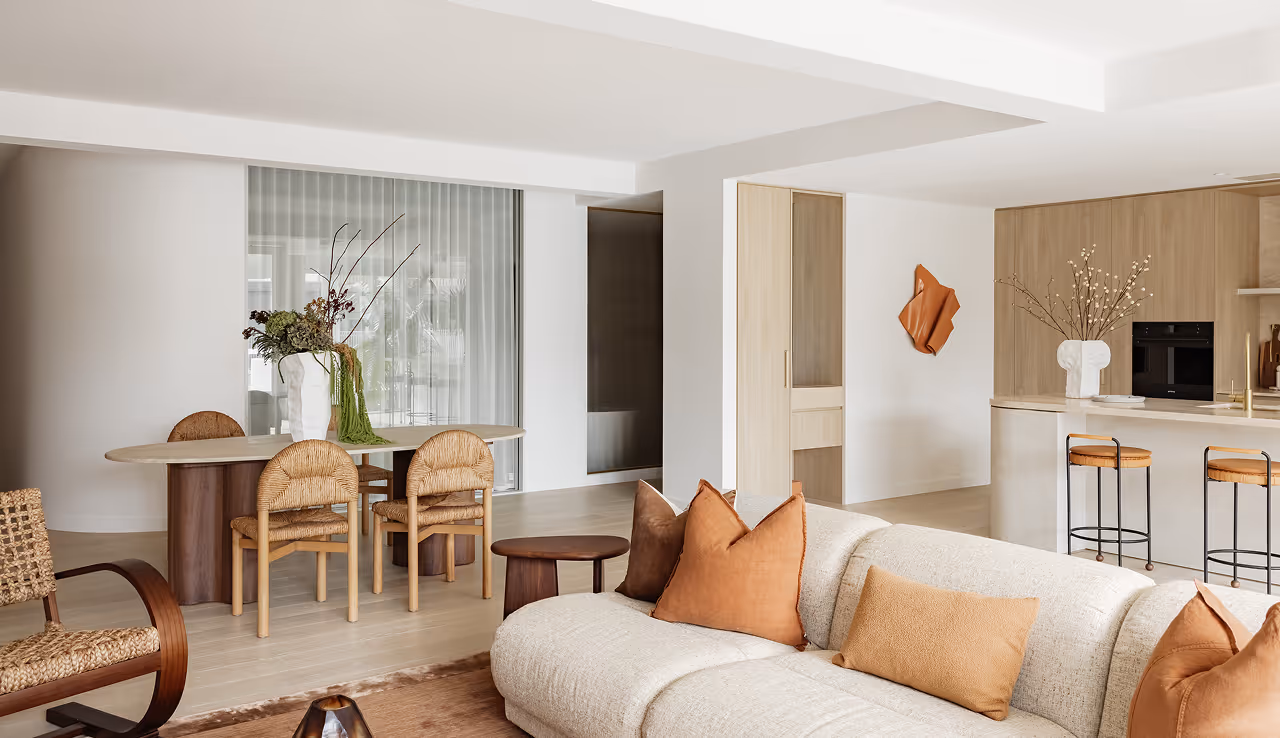 Bright open living room with beige sofa, rust pillows, round dining table, and kitchen island with stools.