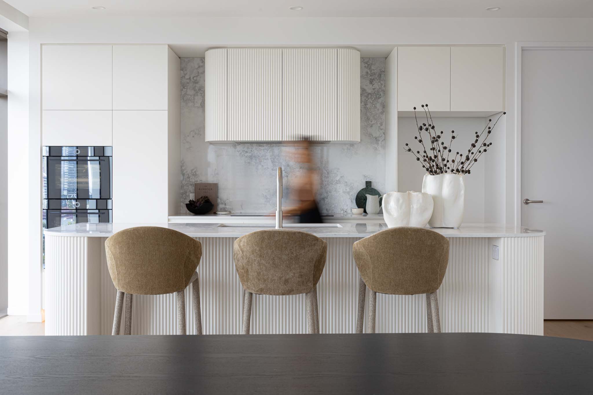 Light wood dining table with modern cream chairs and ceramic vase with dried branches near sheer white curtains.