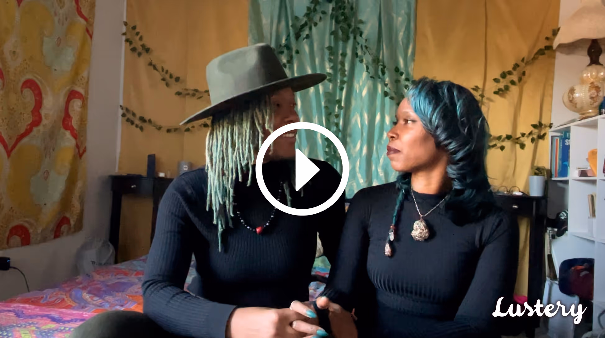 Divine Rae & Godis Meaux wearing black long-sleeve shirts on their bed smiling at one another