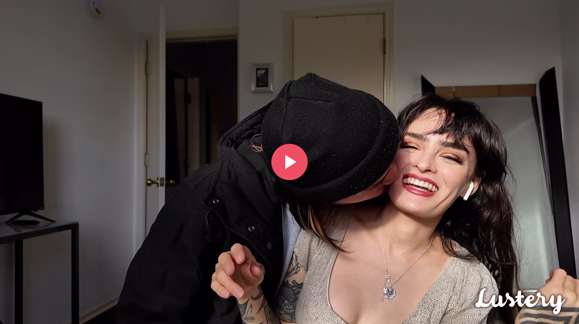 Holly Beth smiles at the camera with airpods in while Hairy Styles wears a black beanie and kisses her on the cheek.