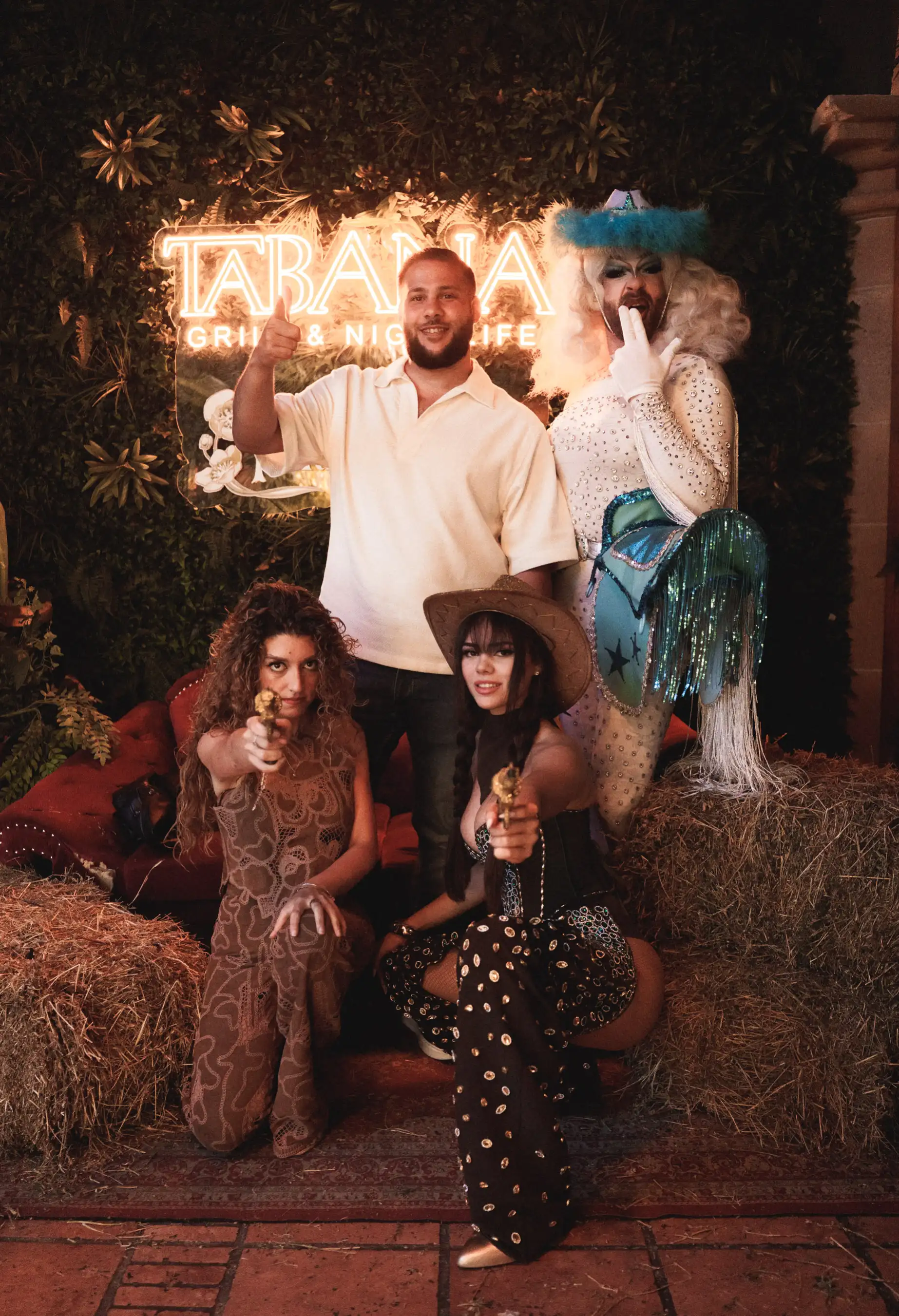 Guests posing with themed performers – Group photo of guests with rodeo-inspired entertainers dressed in glamorous western and drag outfits.