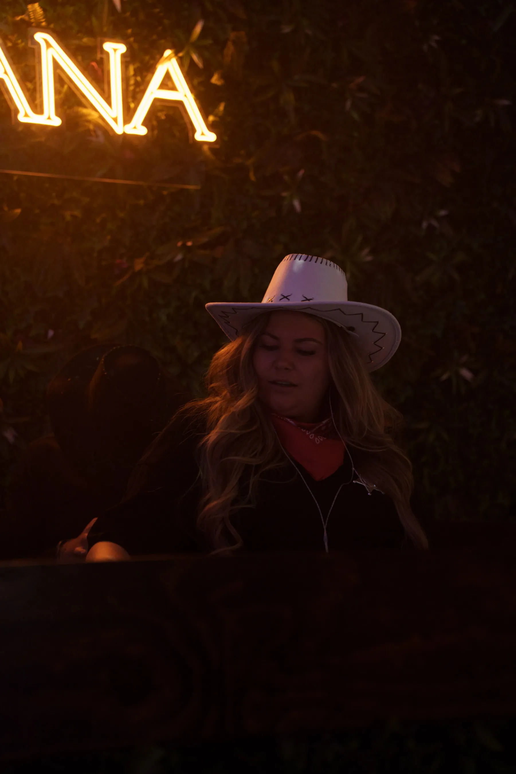 DJ in cowboy hat – Female DJ in western-inspired attire mixing tracks under the neon Tabana sign.