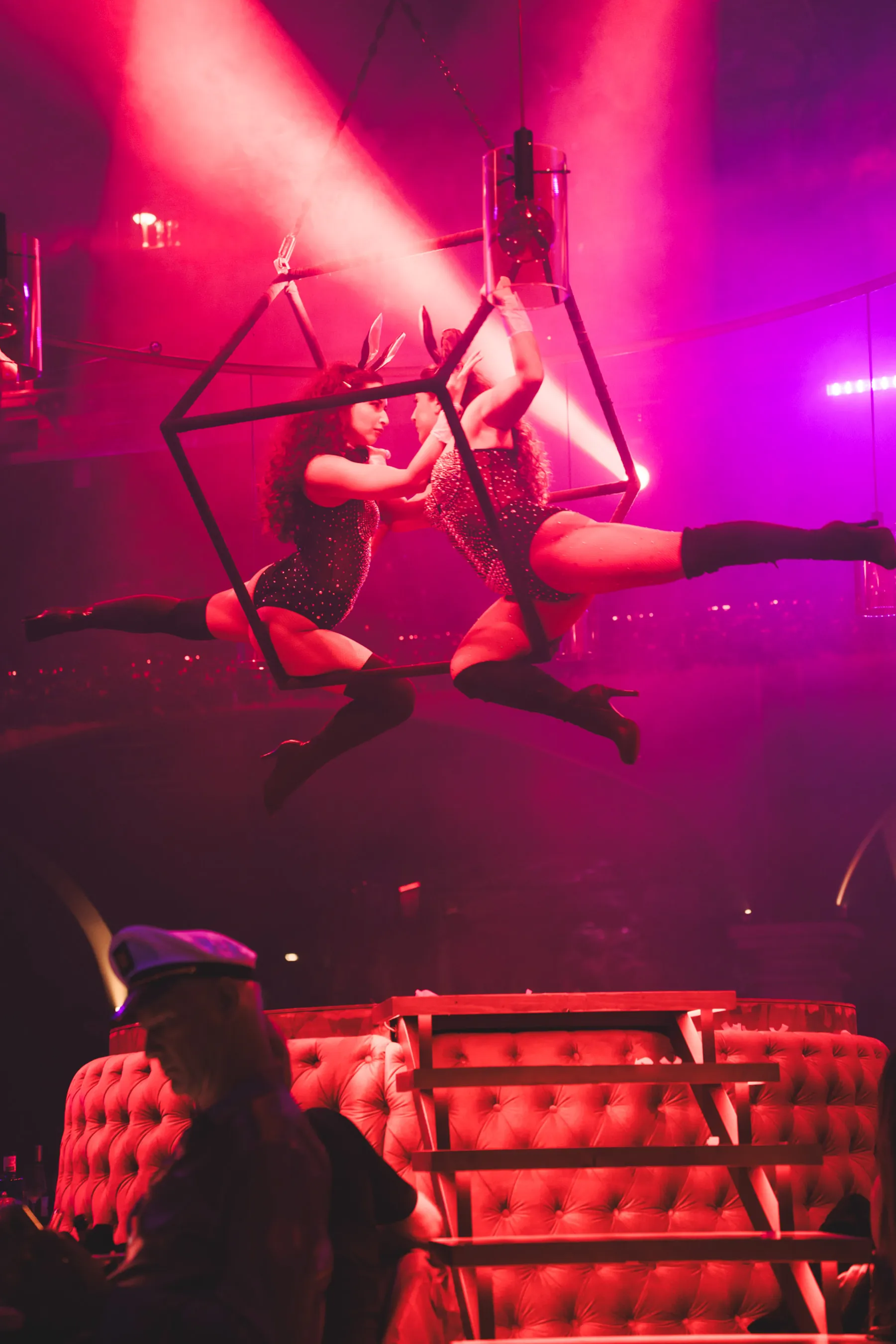 Two aerial performers in bunny costumes suspended mid-air under pink stage lights.