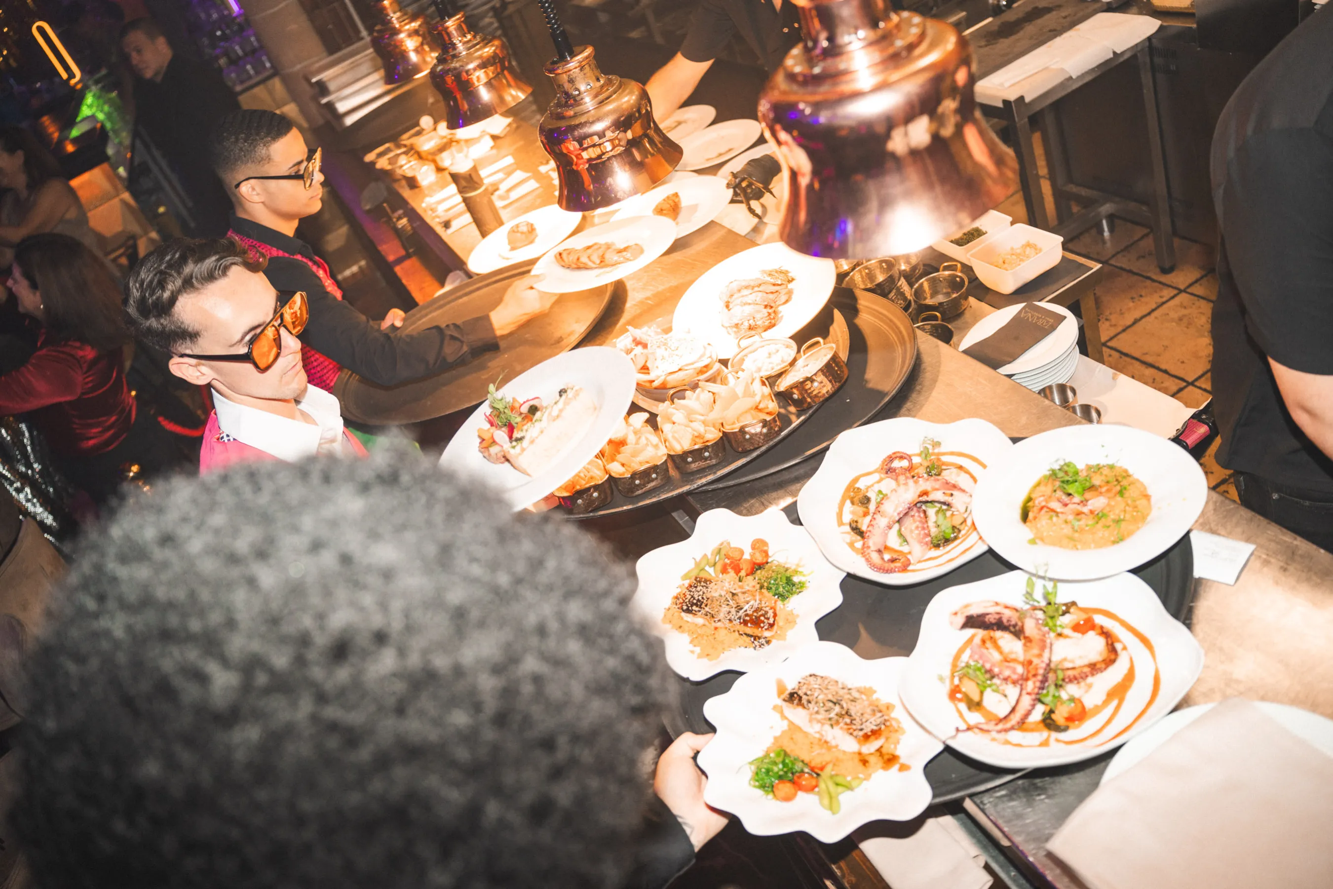 A man holds a tray filled with assorted Mediterranean and Japanese fusion dishes, showcasing Tabana's culinary offerings.
