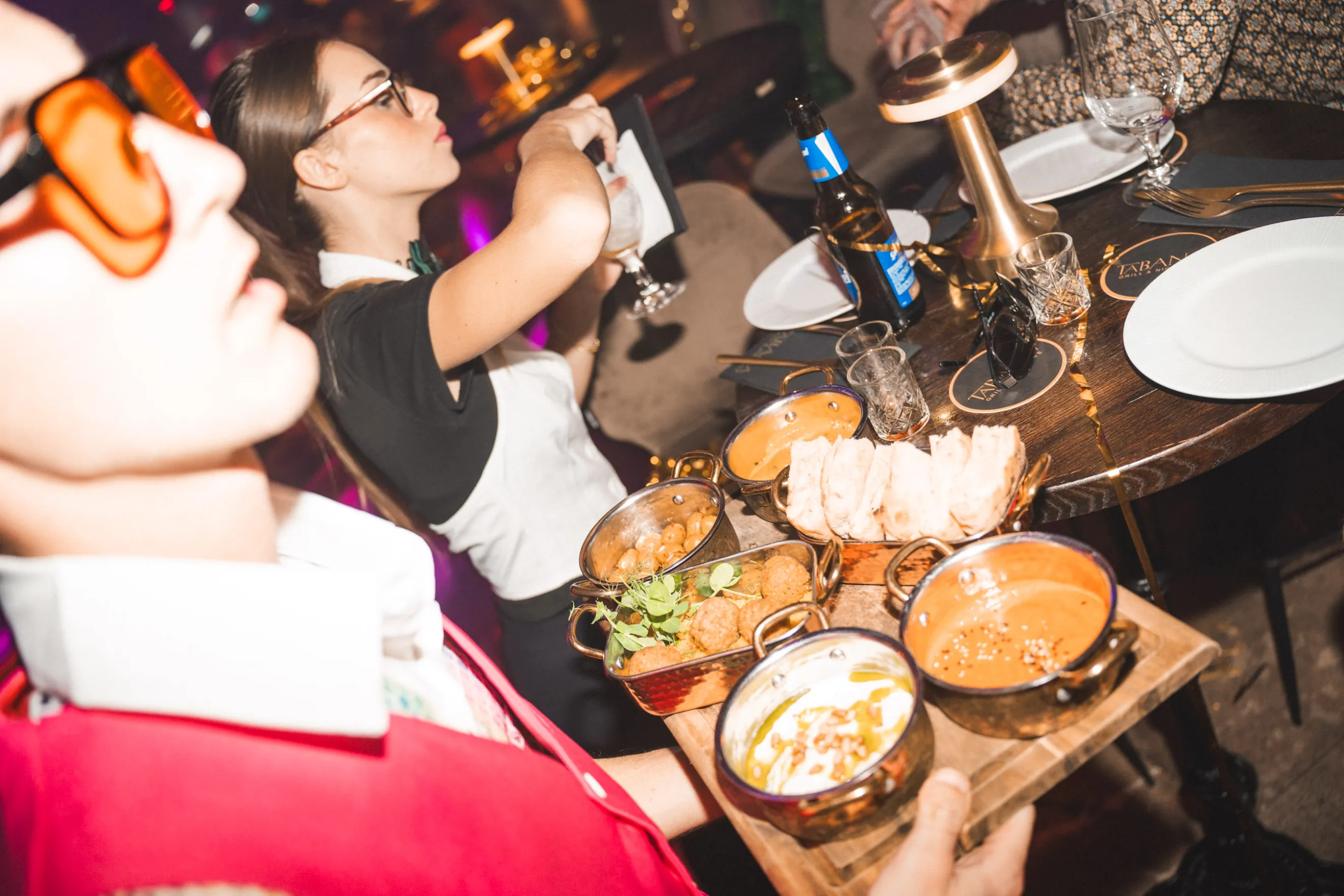 A waiter presents a delicious meal to guests at a lively restaurant, showcasing the dining experience at Tabana.