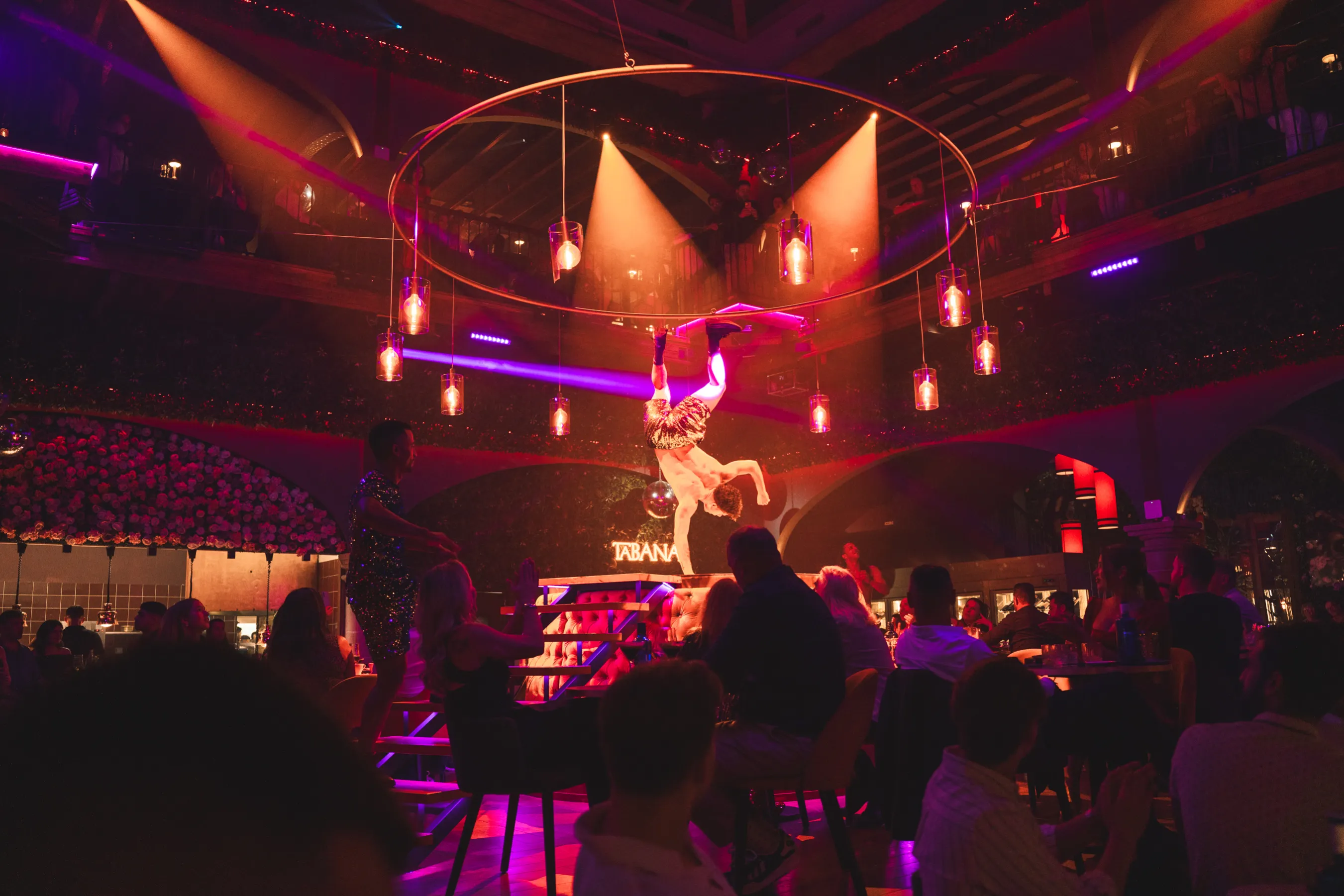 Un habilidoso trapecista deslumbra al público de los clubes nocturnos con una impresionante actuación aérea bajo luces de colores en Tabana