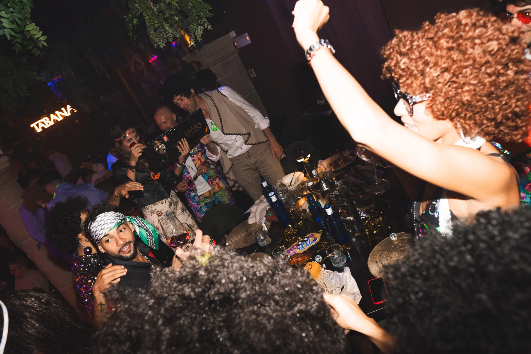 A woman with curly hair celebrates with friends at Tabana, a restaurant known for its lively atmosphere and great food.