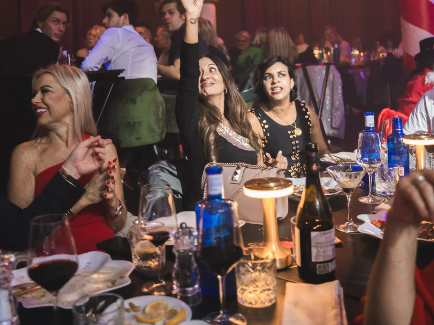 Guests enjoy dinner with wine glasses at a table, while a man in a suit adds elegance to Tabana's dining and nightlife experience.