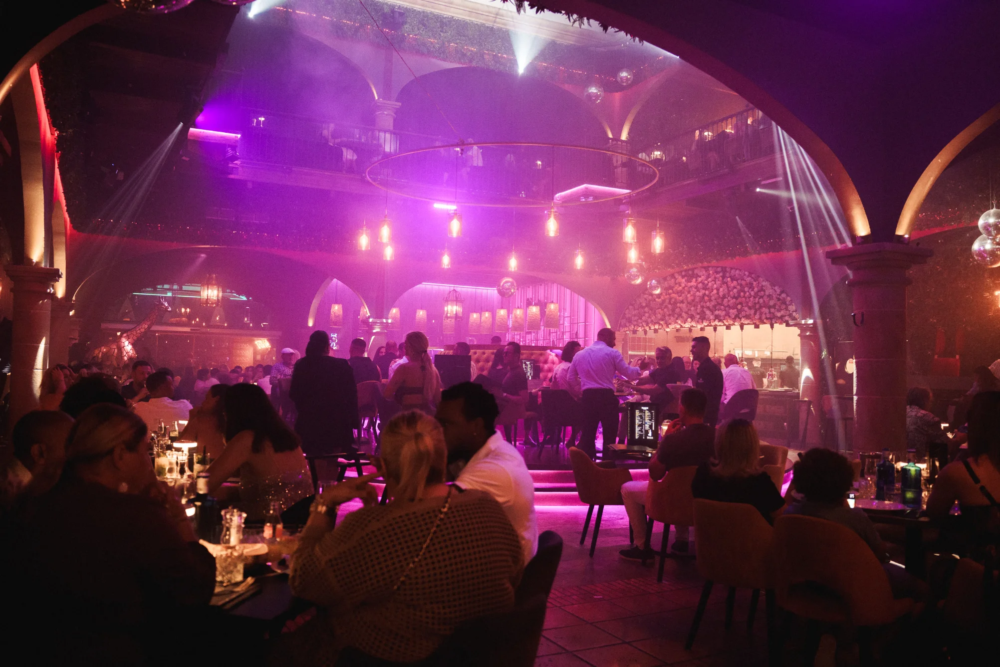 Una animada escena de restaurantes con un gran grupo de invitados que disfrutan de una cena en mesas, anticipando una noche de cena y actuación en vivo.