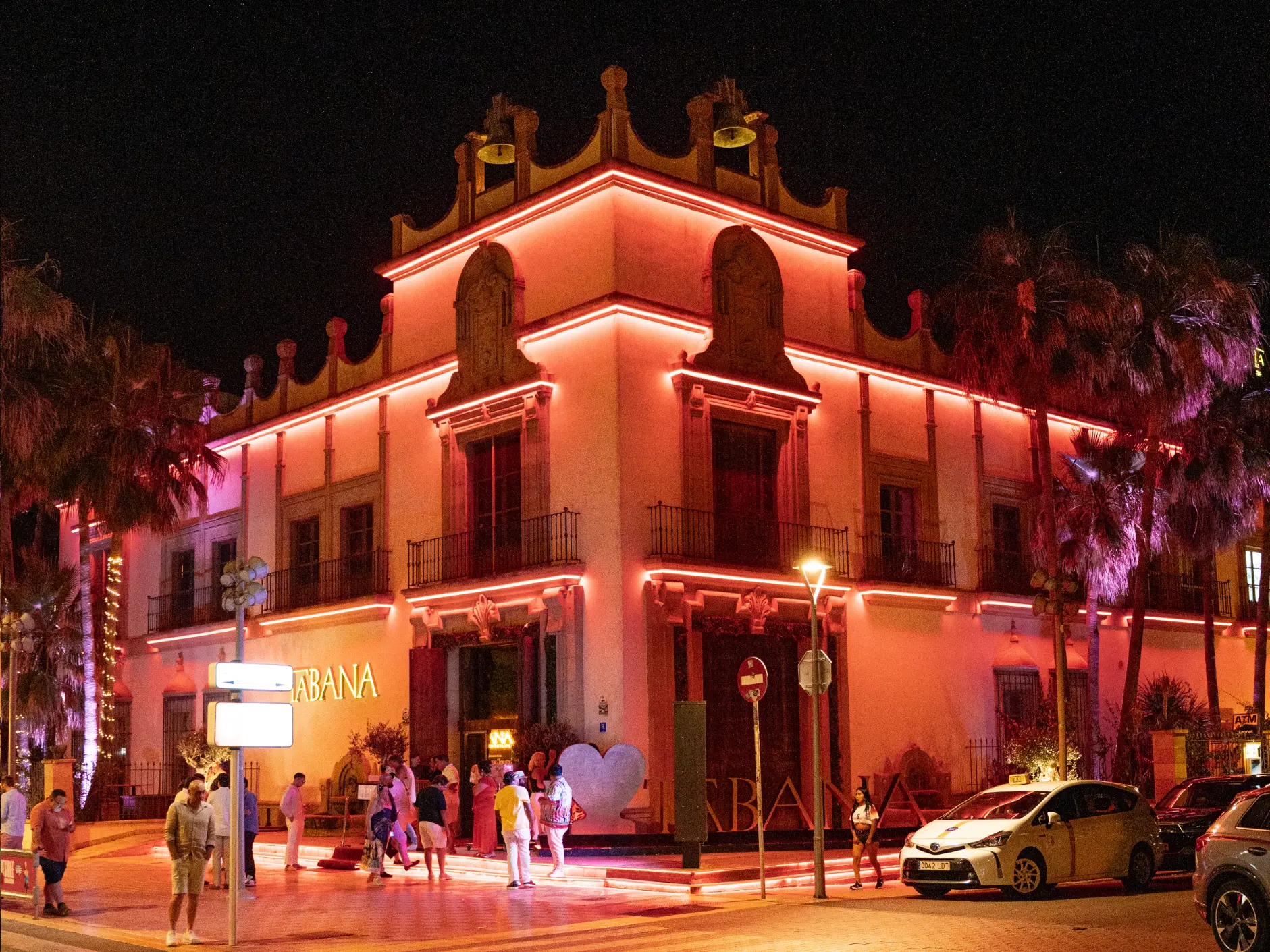 Neon-lit exterior of Tabana dinner show restaurant at night, with guests arriving on the corner in Playa de Palma, Mallorca