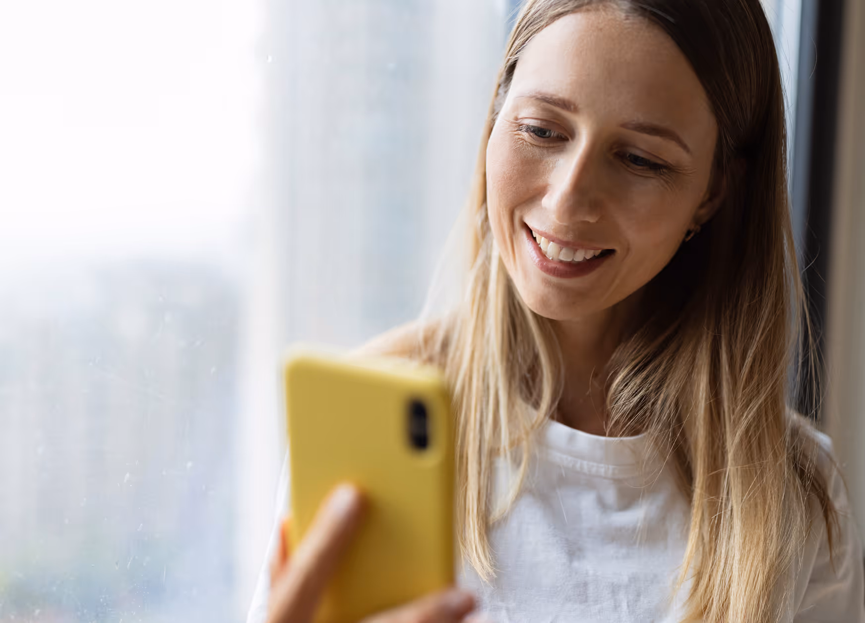 Junge Frau lächelt, während sie auf ihr Smartphone blickt.