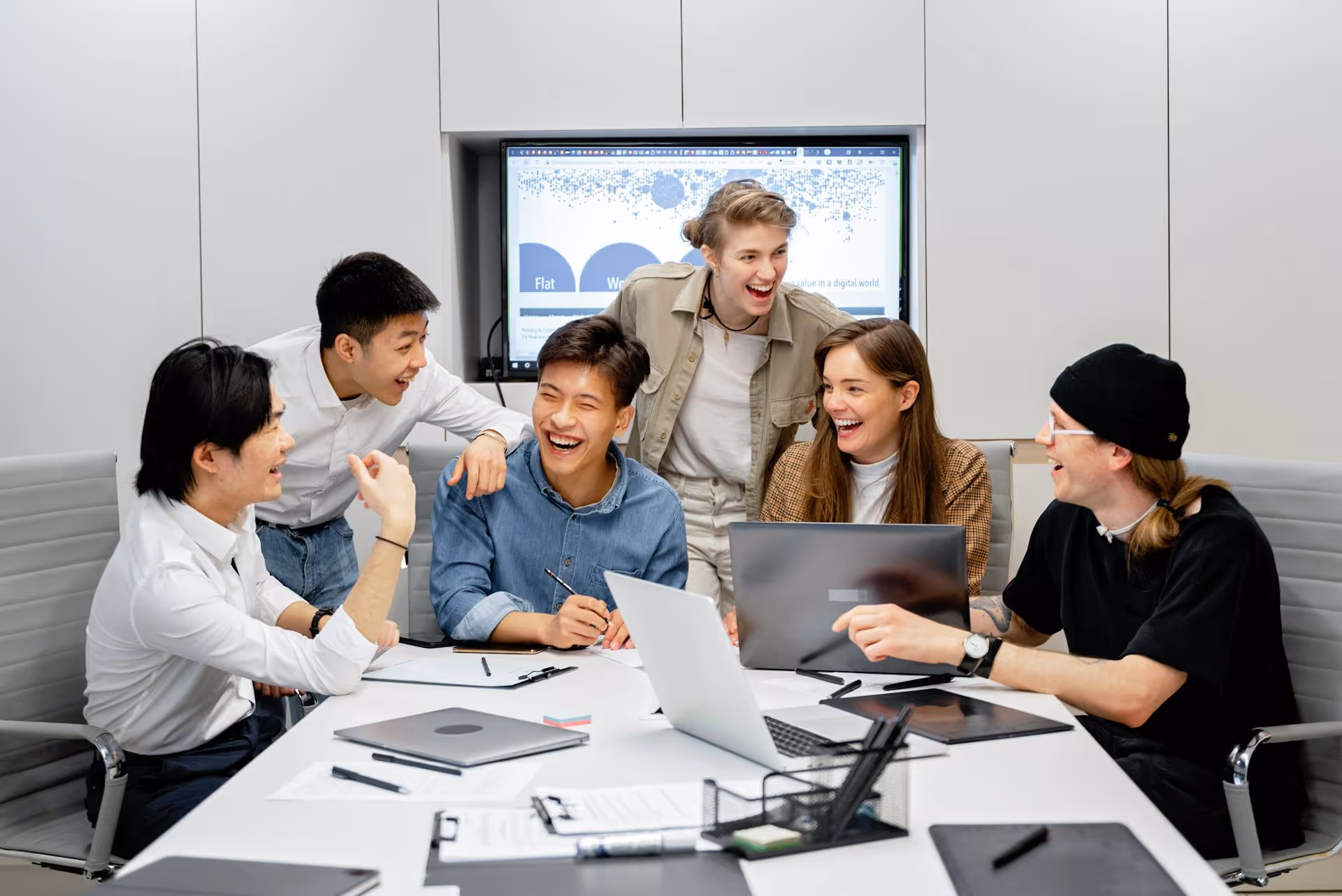 Young people laughing around an office meeting desk and TV.