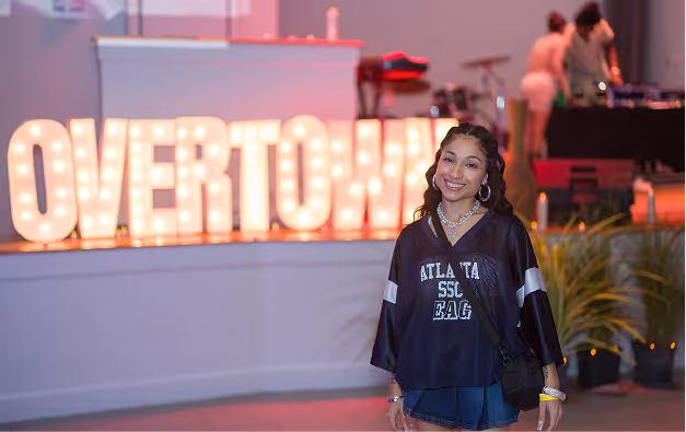 Smiling guest poses in front of lighted Overtown sign at Performing Arts Center event