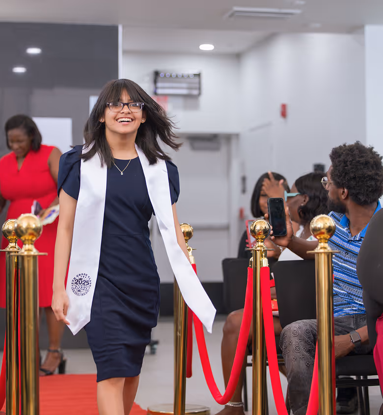Graduate in navy dress walks red carpet during Overtown Performing Arts Center ceremony