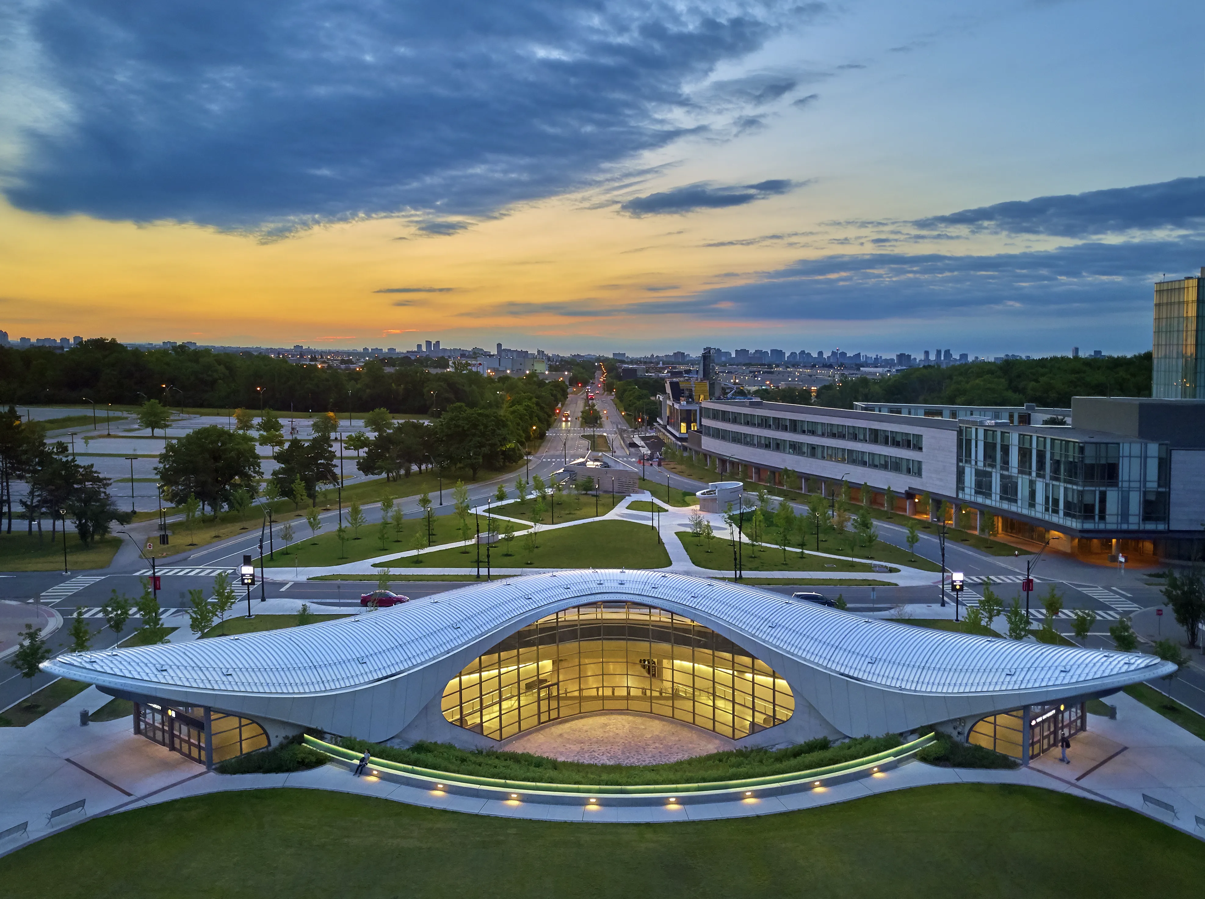 Aerial view of the completed station with its distinctive curved roof centered within landscaped pathways and surrounding campus buildings.