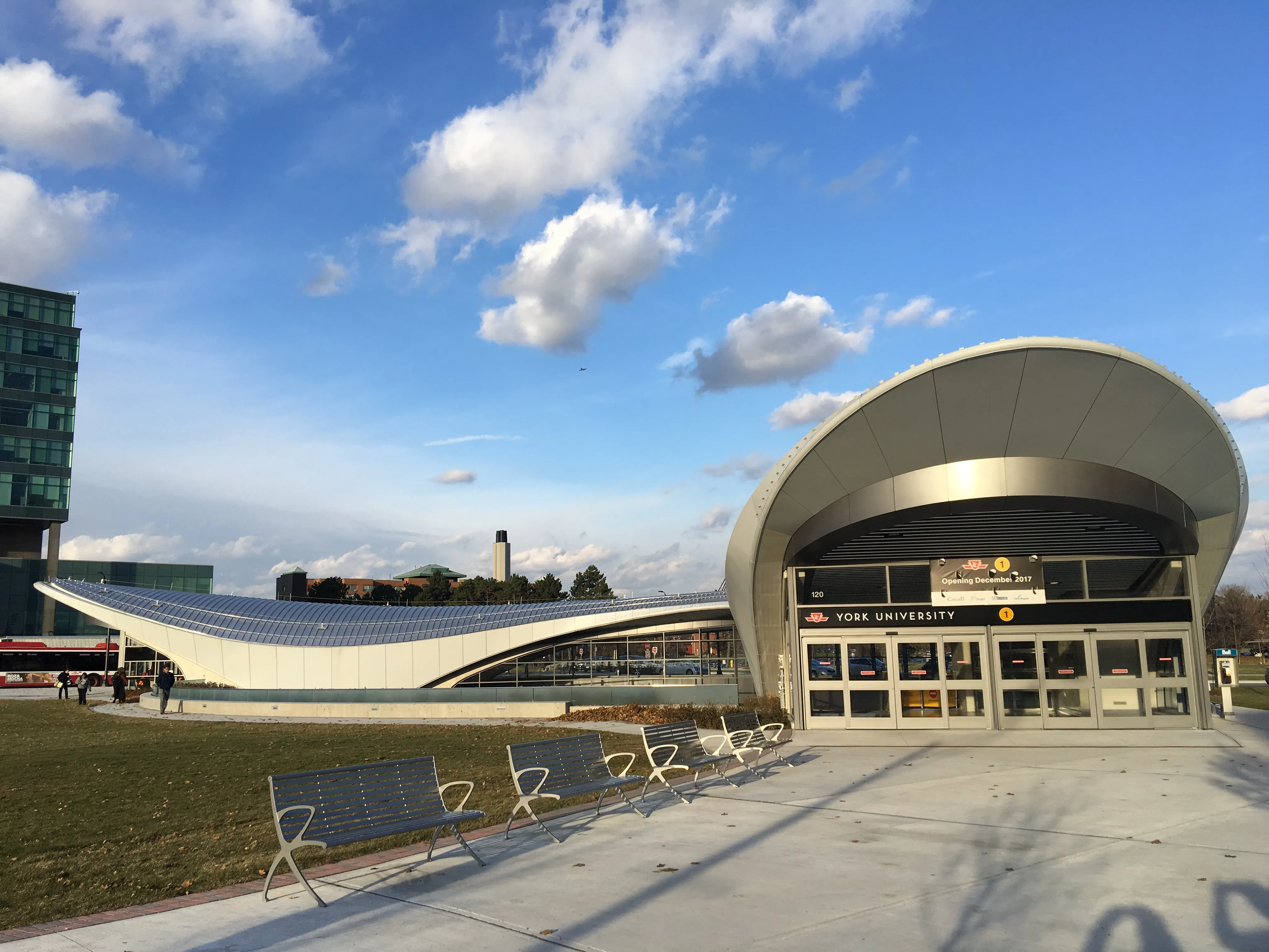 Station entrance with a large curved metallic canopy and glass doors, showing the finished freeform roof structure set by the cold‑formed steel framing system.