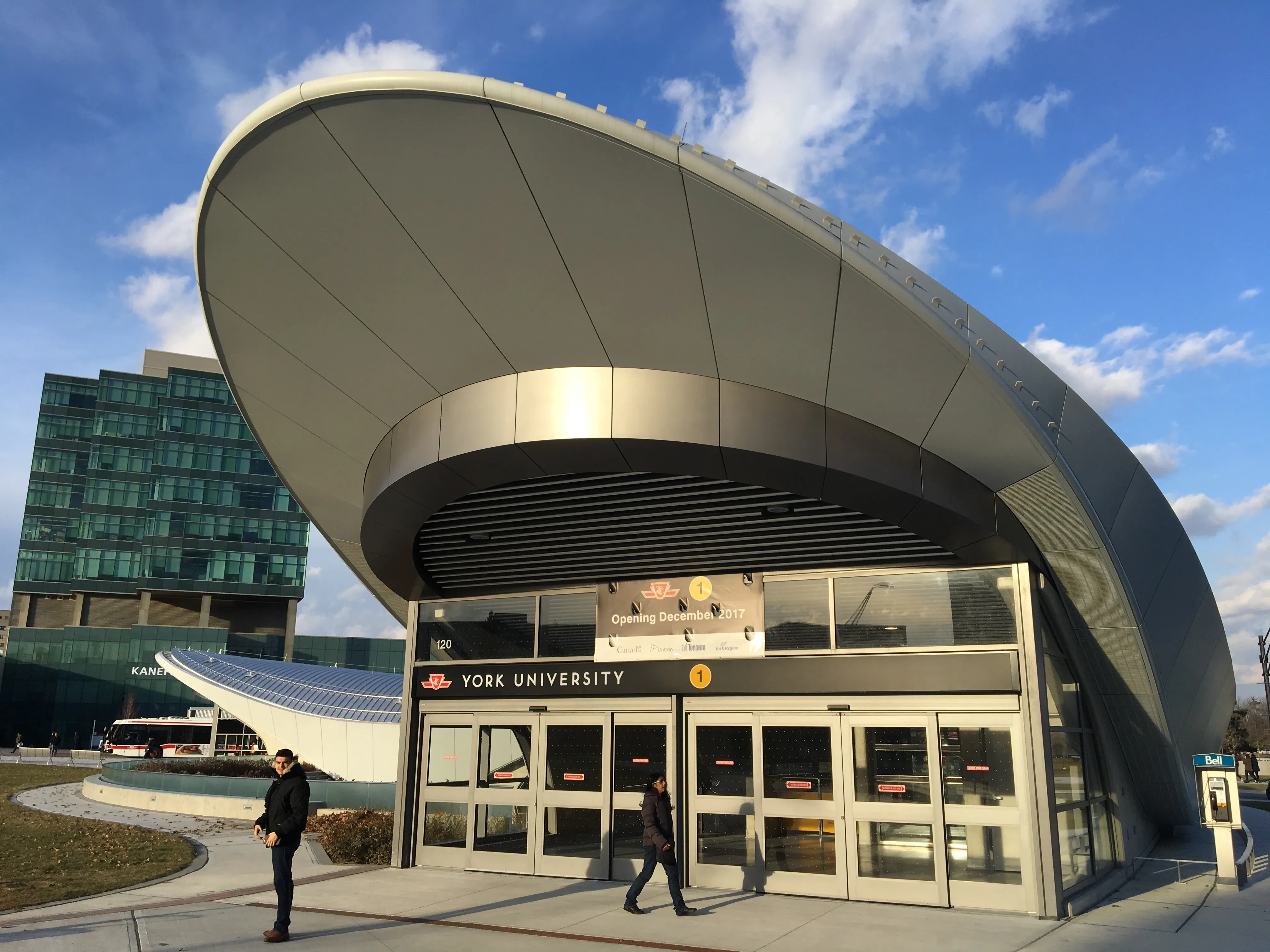 Entrance to a transit station featuring a sweeping curved metal roof and glass façade, illustrating the completed compound‑curve roof geometry.