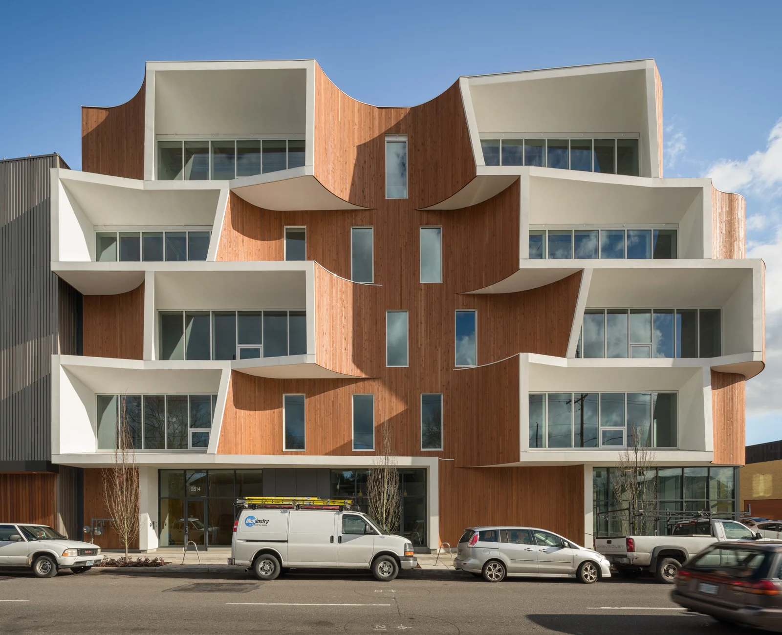 Street‑level view of a multi‑story building featuring wood paneling and angular white apertures projecting from the façade.