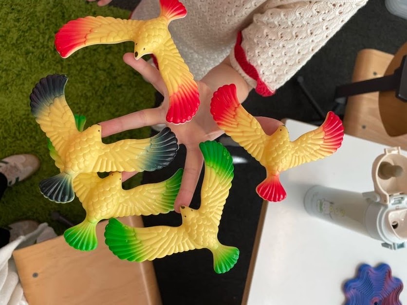 Child holding five yellow toy birds with red, green, and black painted wing tips indoors.