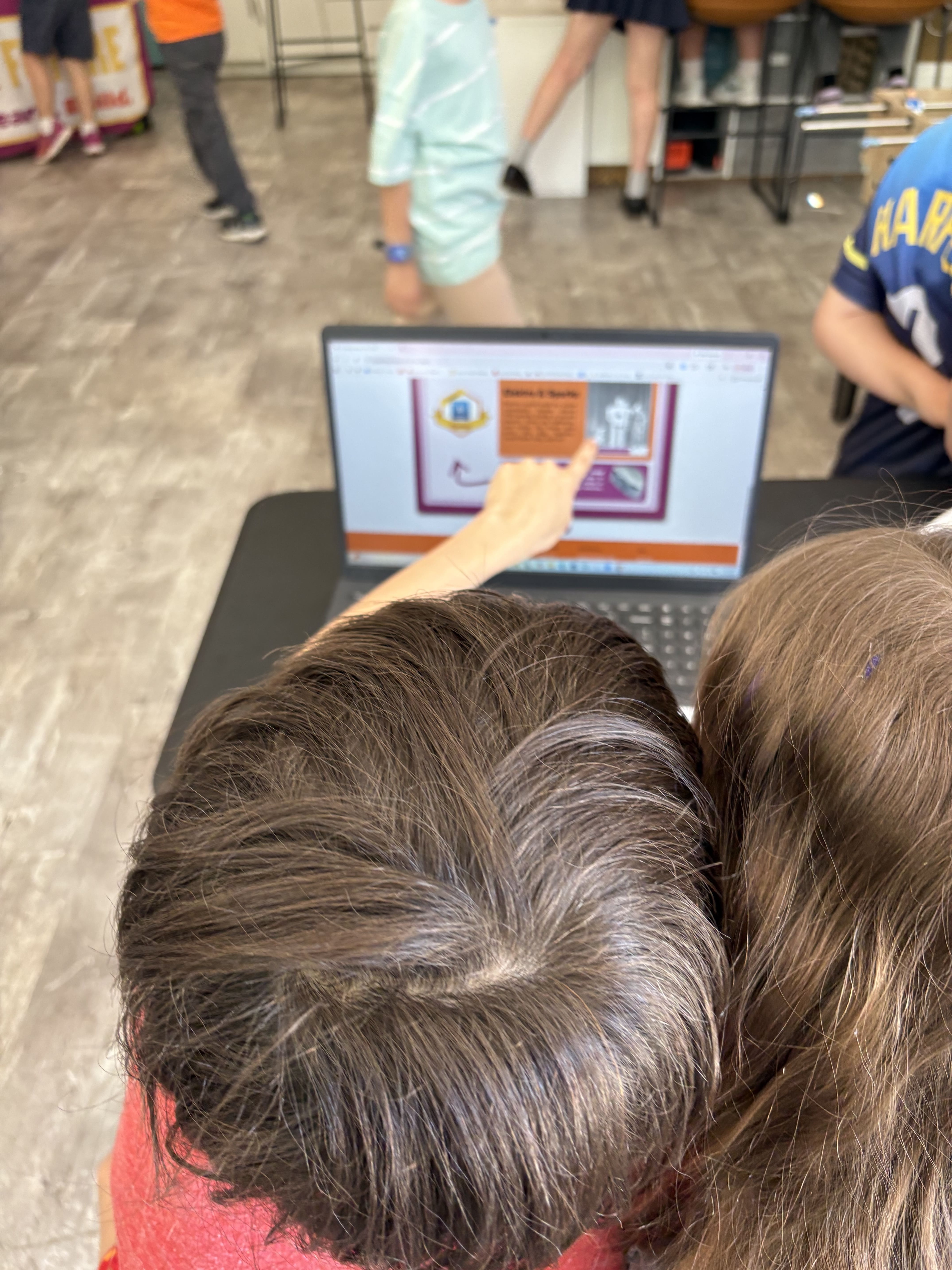 Two children closely looking at a laptop screen, one pointing at content on the screen.