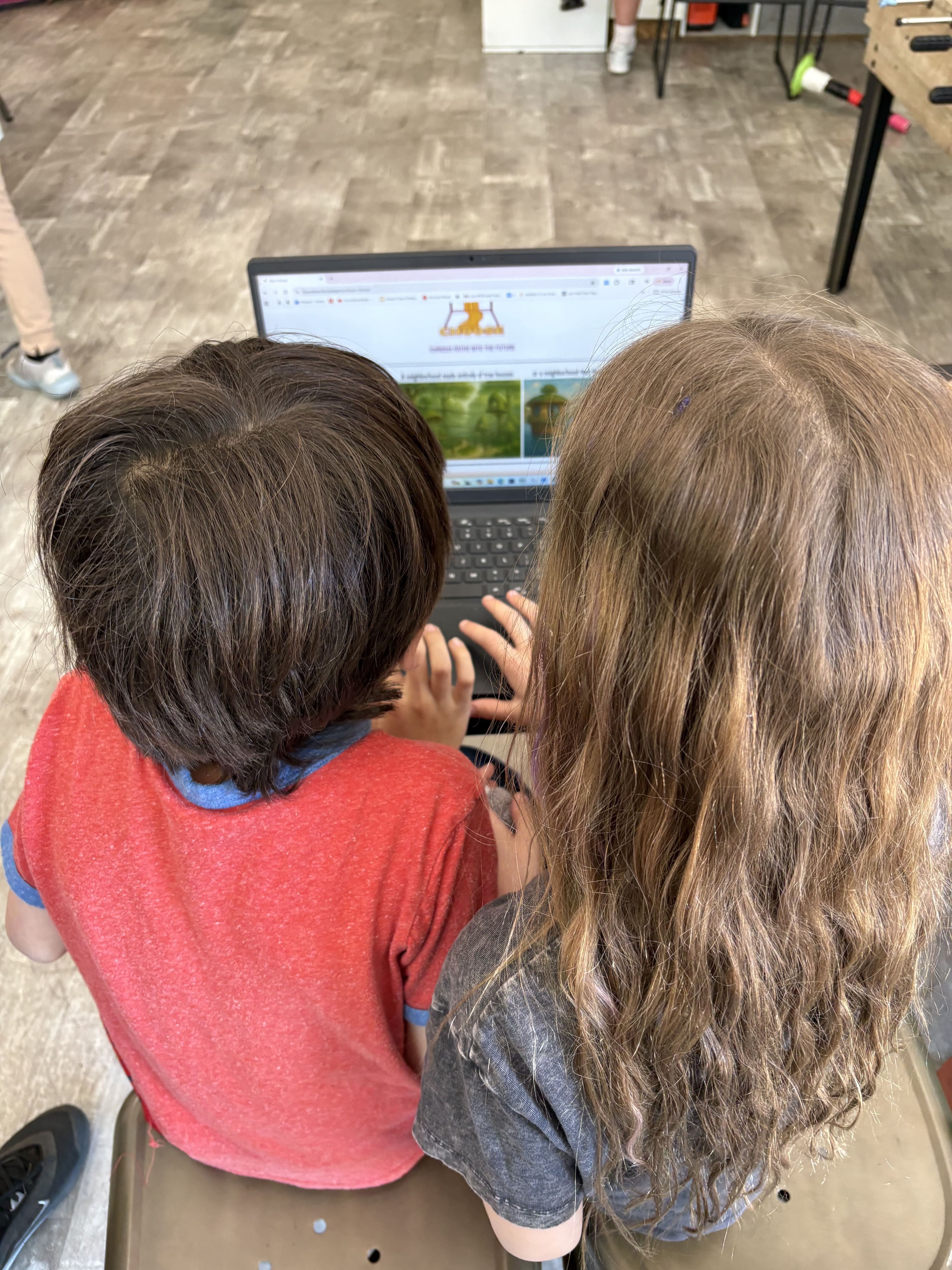 Two children sitting side by side looking at a laptop screen together in a classroom.