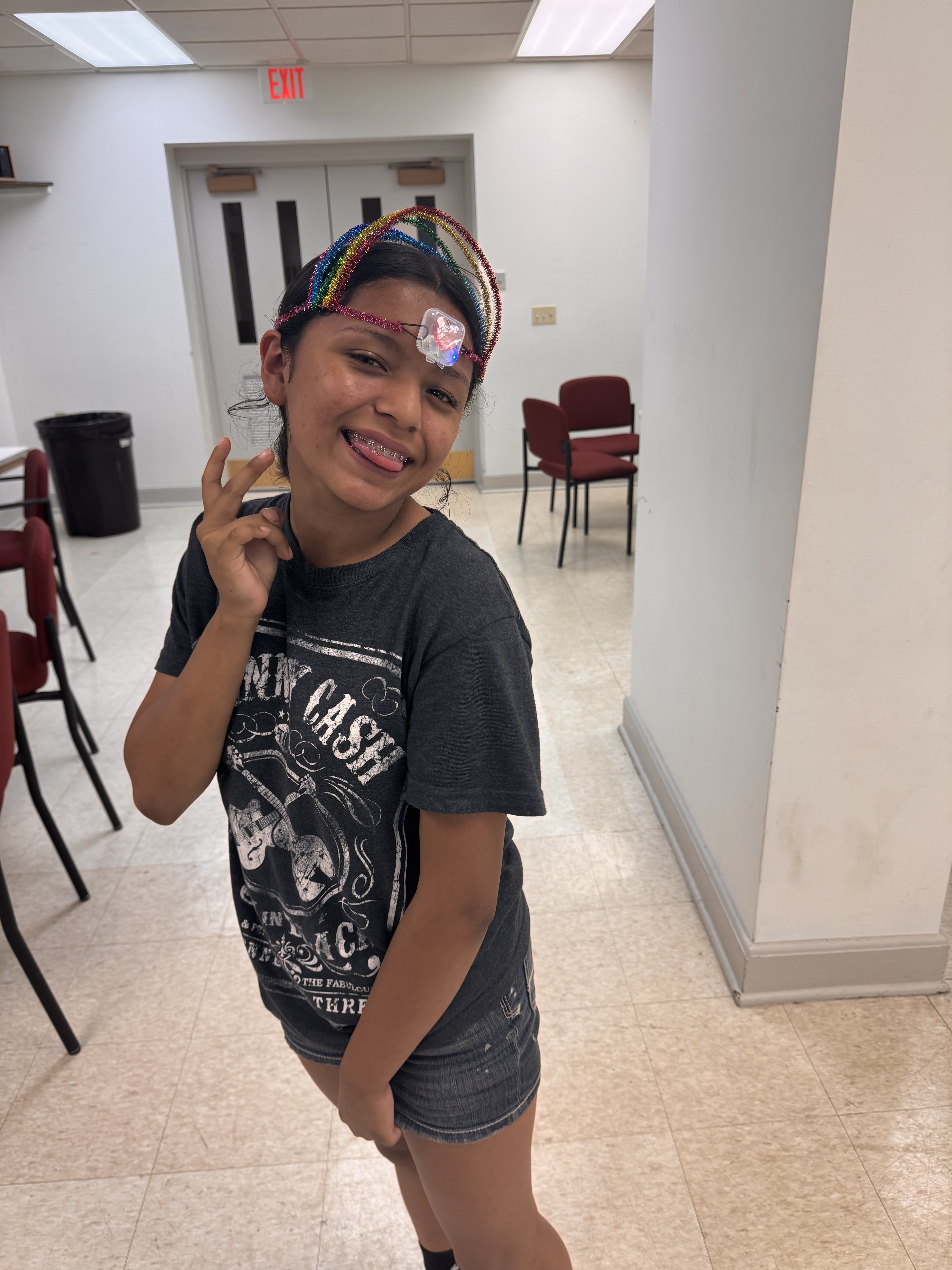 Smiling girl with braces wearing a rainbow headband and dark t-shirt posing inside a room.