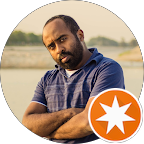 Man with short hair and beard wearing a blue polo shirt, standing outdoors with arms crossed.
