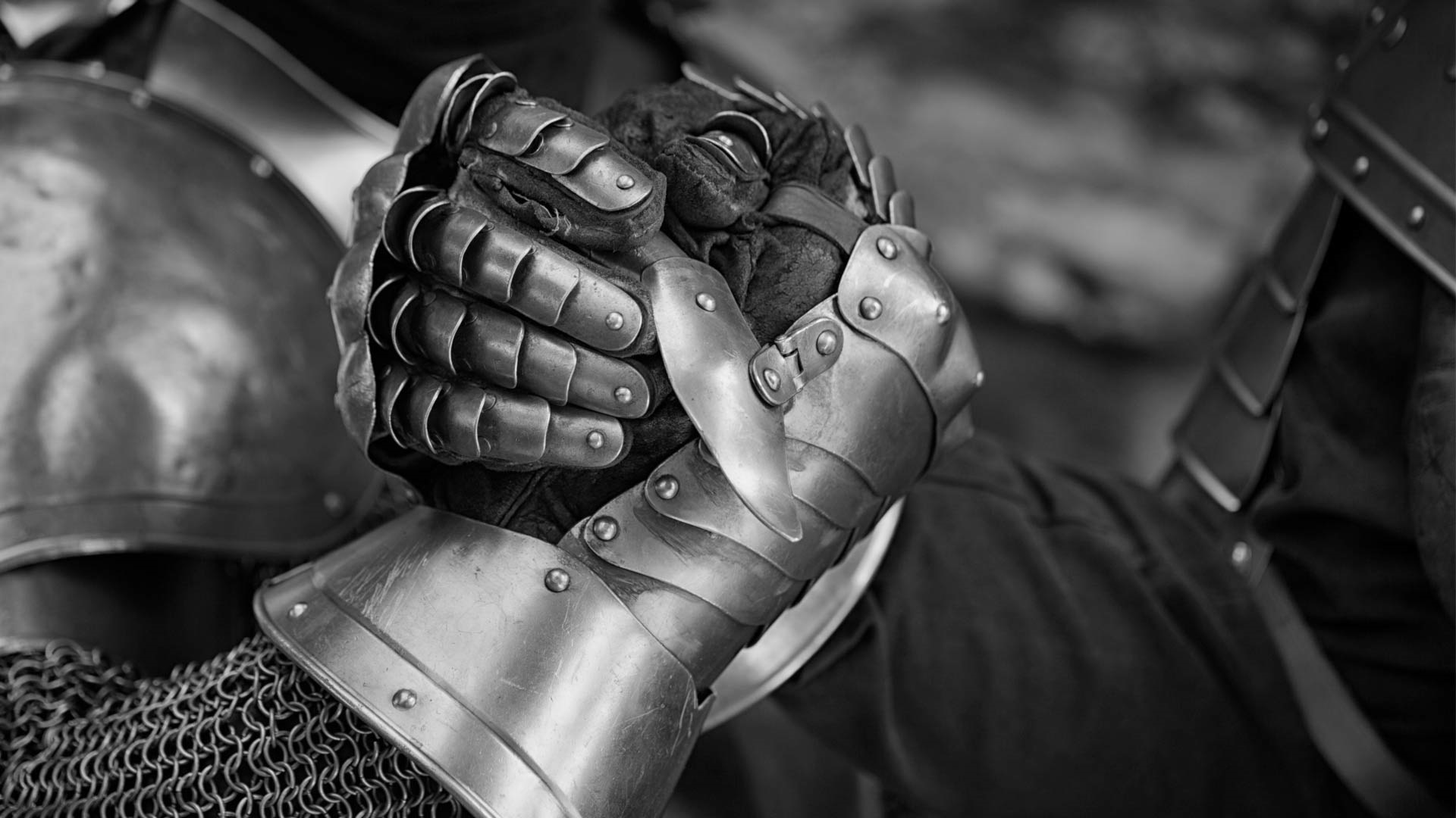 Black and white close-up of two people wearing metal gauntlets clasping hands, symbolizing unity, strength, and solidarity.