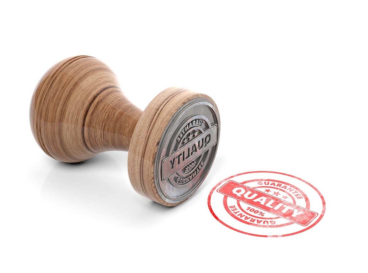 Wooden and metal rubber stamp with the word ‘QUALITY’ next to a red circular stamp mark reading ‘100% Quality Guarantee.