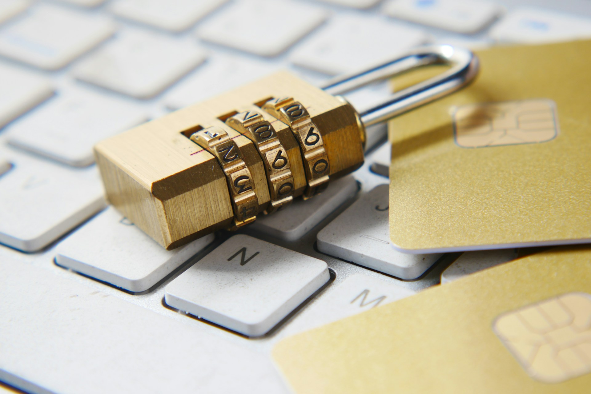 Close-up of a combination padlock placed on a computer keyboard next to gold credit cards, symbolizing cybersecurity and data protection.
