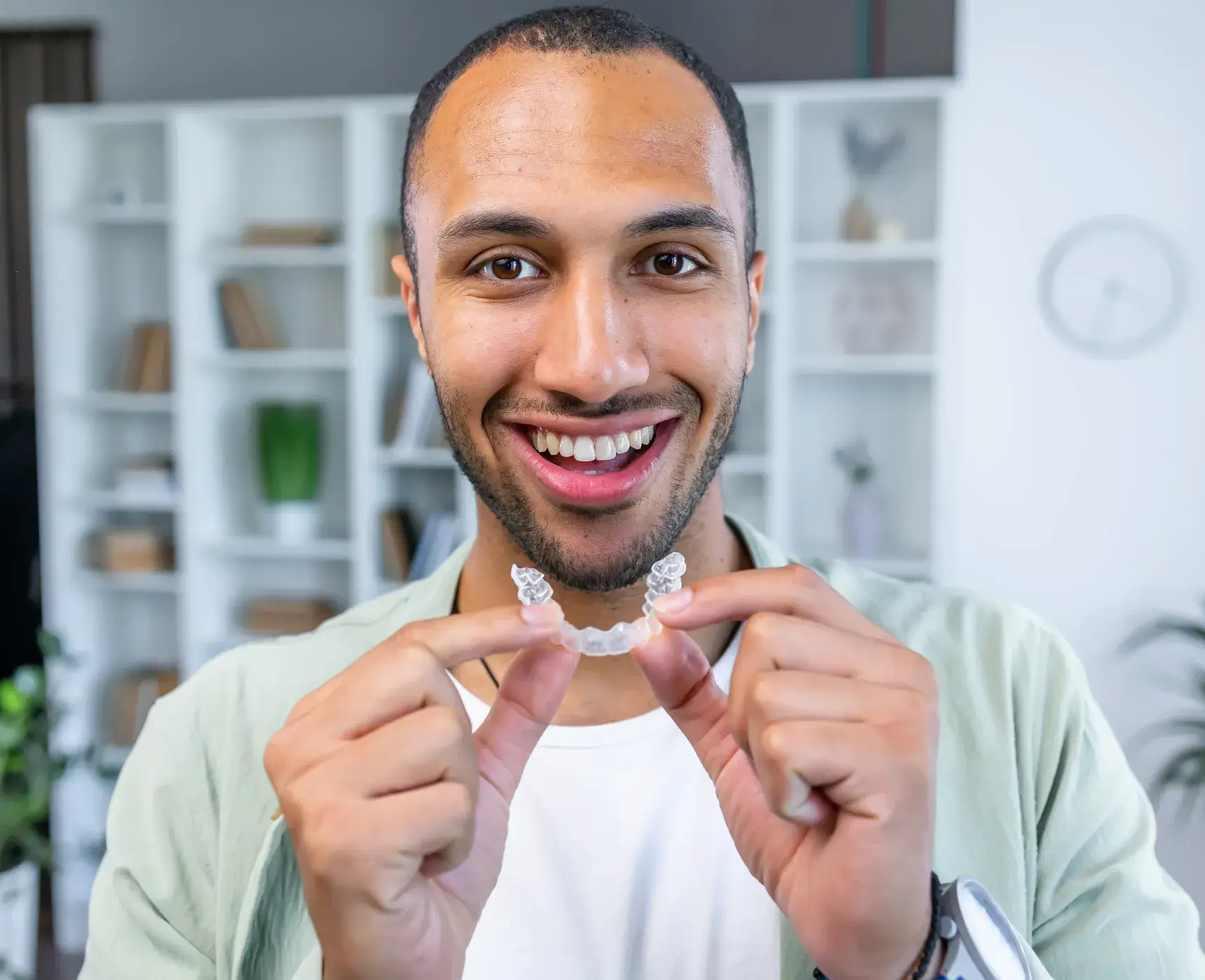 A man smiles while holding a toothbrush in his hands.