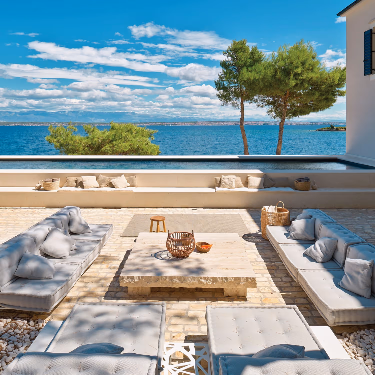 Services, maintain, rent or sell your property. Image showing a seaside Villa’s terrace with a stone coffee table surrounded by comfortable sofas. There is a swimming pool at the end of such terrace. In the background one sees a beautiful Mediterranean Sea panoramic view in a bright and sunny summer day.